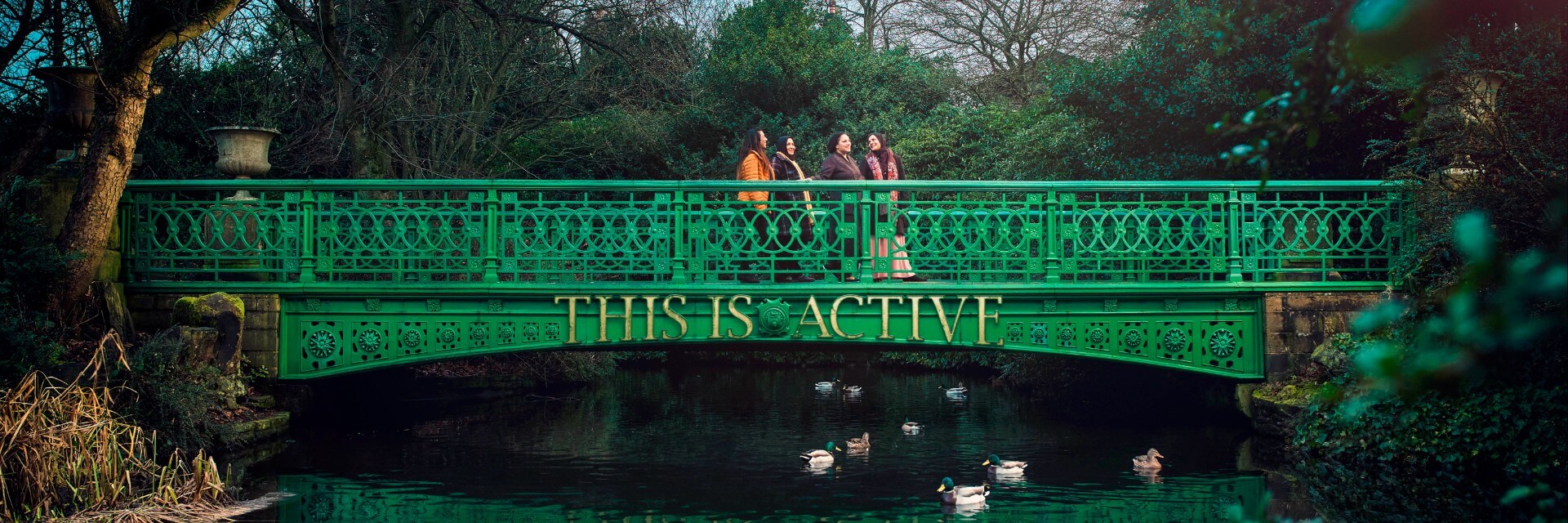 A South Asian Ladies walking group crossing a bridge in People's park. The bridge has the words "this is active" on it.